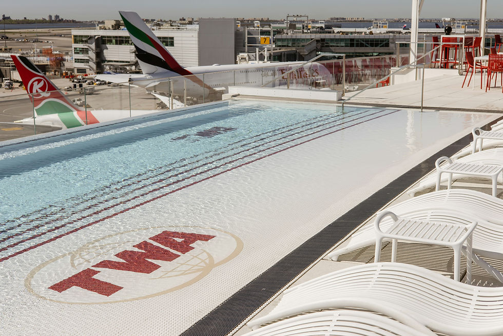 Rooftop pool with TWA logo, surrounded by white lounge chairs. Overlooks airport with red and green plane tails. Clear, sunny day.