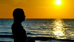 Silhouette of a person gazing at a vibrant orange sunset over the ocean, creating a serene and reflective mood.