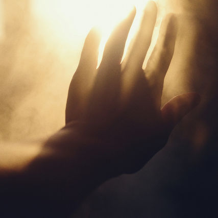 Silhouette of a hand reaching toward bright golden light through warm haze, creating a dreamy, intimate mood.