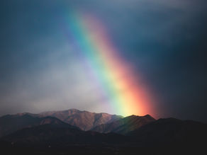 Photo of a rainbow in a dark sky over a mountain range.