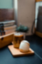 Iced coffee and a cream-filled pastry on a wooden tray, set on a dark countertop with blurred books and a plant in the background.