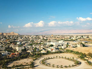 Wide panoramic view overlooking the city buildings and green palm tree groves of the Jericho oasis in the Jordan Valley.