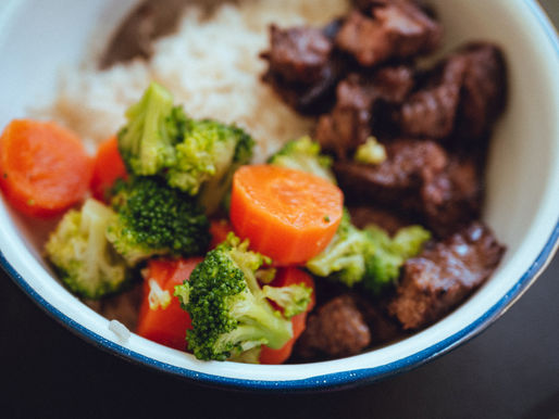 Bowl of rice with beef, broccoli, and carrots, a colorful homemade meal in a white-rimmed dish.