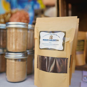 Mushroom coffee bag labeled Organic medicinal mushrooms beside jars of powder at a market stall.