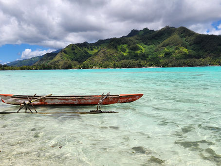 Canoa tradizionale polinesiana su mare cristallino con sfondo isola collinare ricca di vegetazione