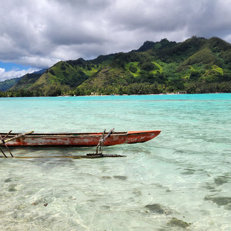 Canoa tradizionale polinesiana su mare cristallino con sfondo isola collinare ricca di vegetazione