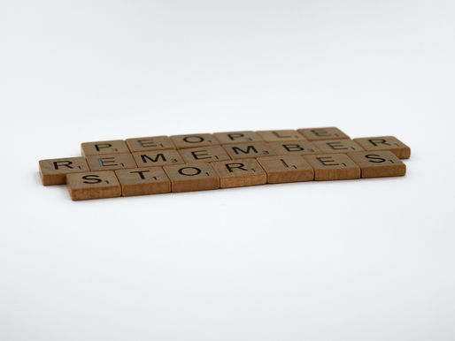Peças de madeira formando a frase "PEOPLE REMEMBER STORIES" sobre fundo branco. Letras pretas em blocos marrons.