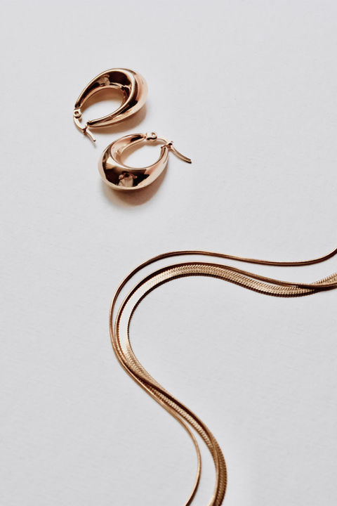 Two gold hoop earrings and a herringbone necklace on a light background.