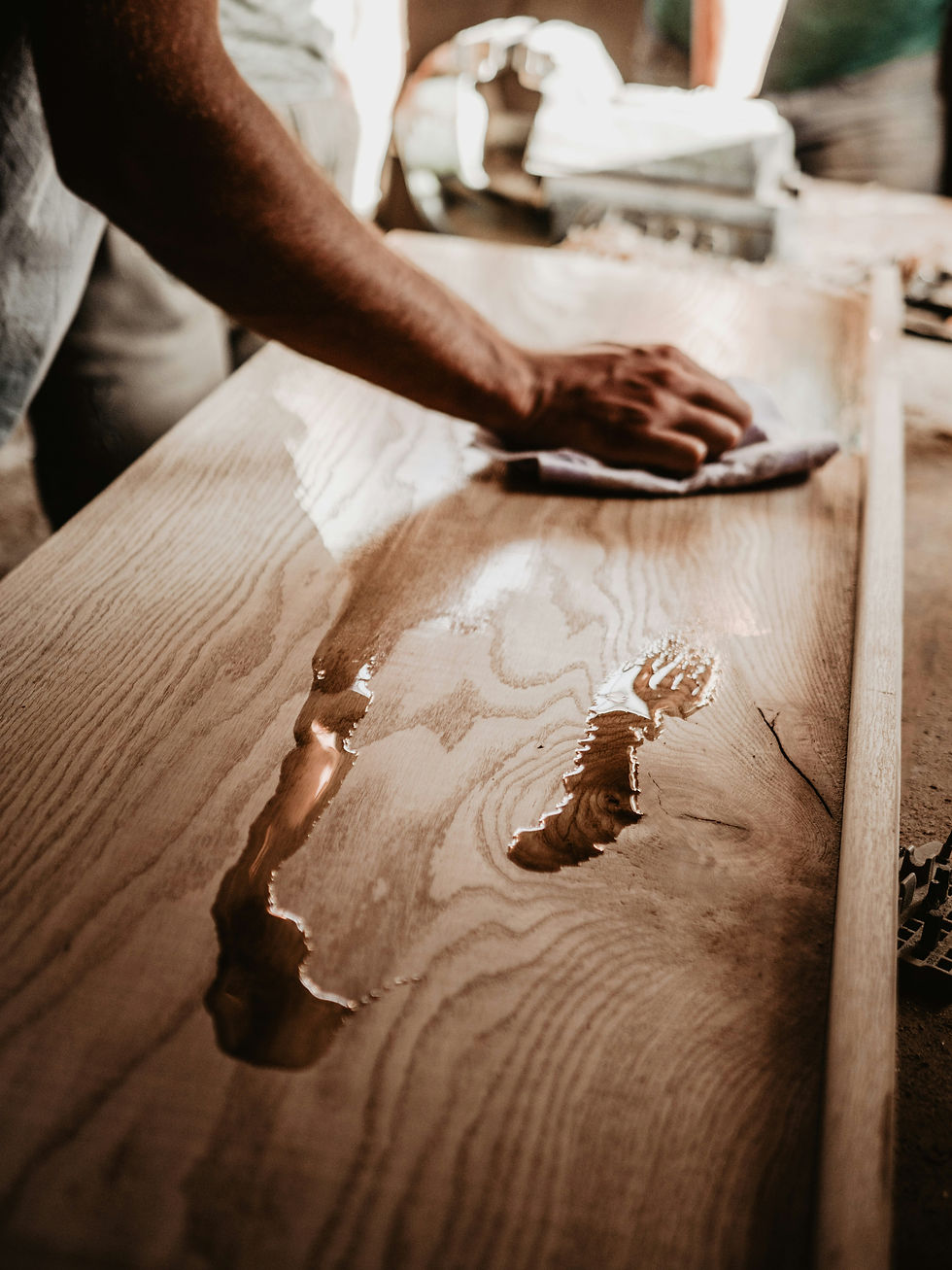 A craftsman meticulously applies a coat of polish to a wooden board, highlighting the natural grain and texture under the workshop's warm light.