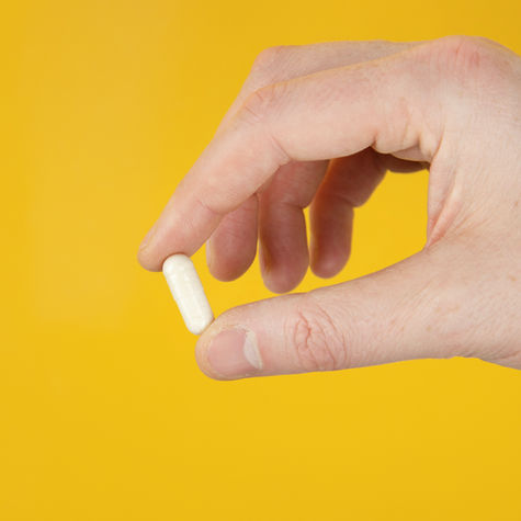 A hand holding a small white pill