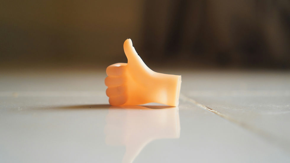 Thumb-shaped object on a reflective surface, giving a thumbs-up. Warm lighting and a blurred dark background.