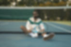 fashionable guy sitting on tennis court against the net holding a racket