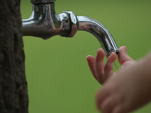 child's hand under an outdoor water spigot