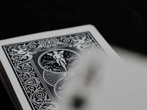A deck of intricately designed black and white playing cards on a dark surface, with a close-up of the card back pattern.