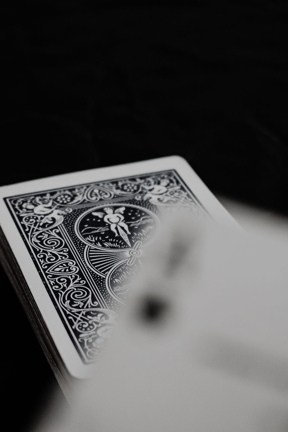A deck of intricately designed black and white playing cards on a dark surface, with a close-up of the card back pattern.