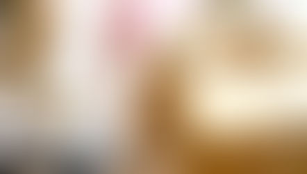 Gift wrapped in brown paper with gold ribbon, alongside scissors on a white surface. A pink ribbon is blurred in the background.