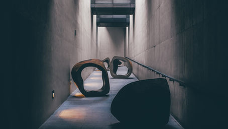 Abstrakte Skulpturen in einem schmalen, betonierten Gang mit wechselndem Licht – symbolisch für einen nicht geradlinigen Weg.