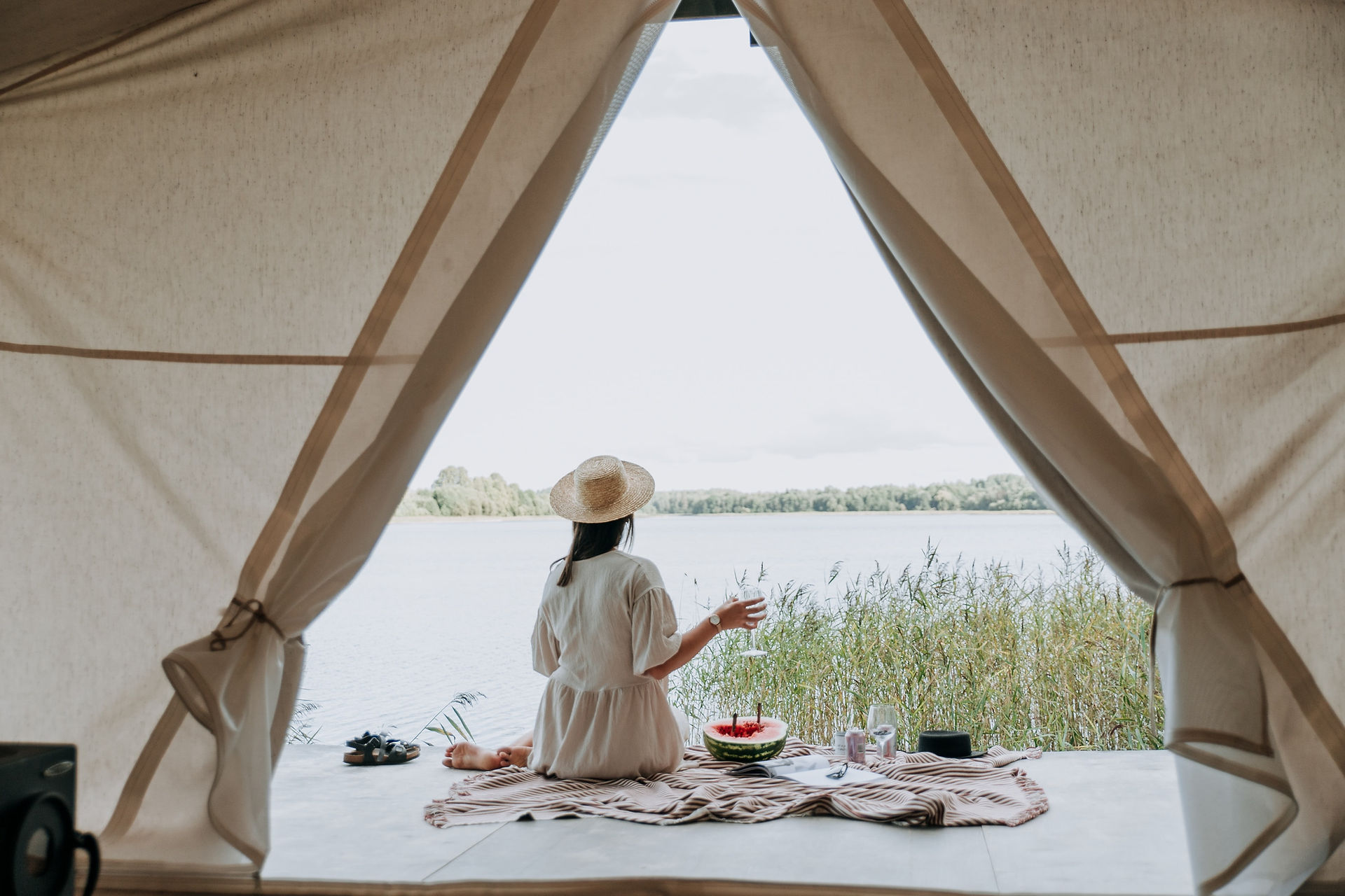 A woman sitting in a bell tent looking at the view of a lake, holding a glass of wine.