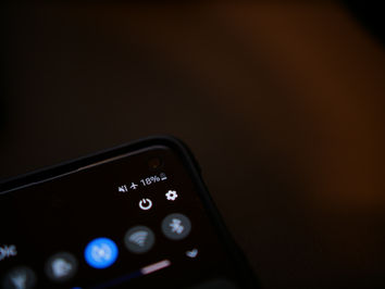 Close-up of a phone screen showing 18% battery, airplane mode icon, and settings gear. The background is dark and blurred.