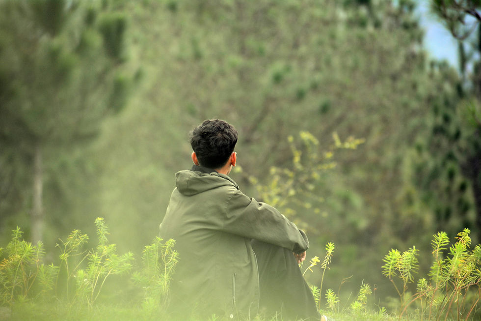 Teen sitting quietly in a natural setting, surrounded by soft greenery, resting in a calm and reflective outdoor moment