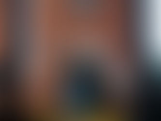 Brick building with a sign reading "Carnegie Free Library" above a blue door. Security camera and signs on walls. Iron railing in foreground.