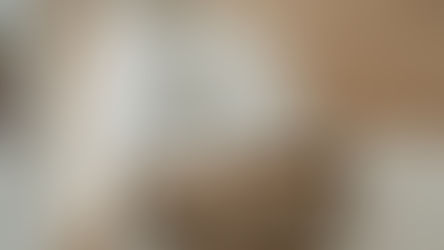 Bathroom with wooden vanity, dual brass faucets, and a round mirror. Slanted wooden ceiling and a jute rug create a cozy ambiance.