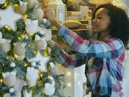 A young woman decorating a Christmas tree with white ornaments 