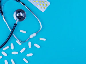 A stethoscope on a blue surface along with some antibiotics.