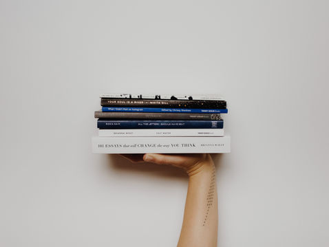 Hand holding a stack of six books against a white background, including 101 Essays That Will Change the Way You Think.
