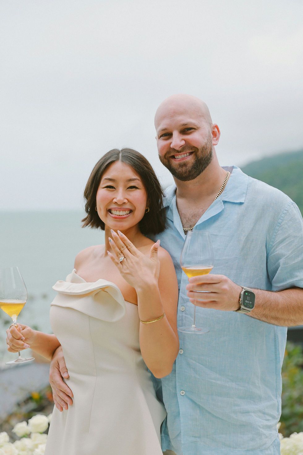 A smiling couple holds glasses of champagne just engaged, engagement, wedding venues in Spartanburg, outdoor wedding ceremony, garden wedding in Spartanburg, all inclusive wedding venue near me, wedding venues in Upstate South Carolina