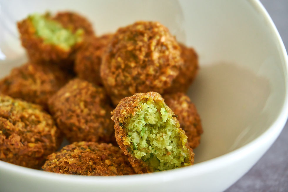 A closeup of a bowl of falafel balls with one broken open to show a green interior