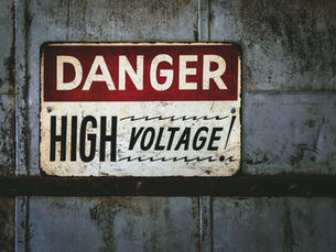 A weathered "Danger High Voltage" sign on a rusty metal wall, with bold red and black text warning of electrical hazards.