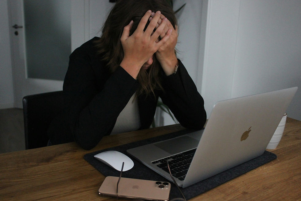 Overwhelmed woman with her head in her hands sitting in front of a laptop.