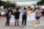 An image of 4 people holding up a sign with more signs in the background displaying their non profit support for pride.