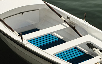 Small white fiberglass rowing boat with wooden oars and blue slatted floorboards floating on water