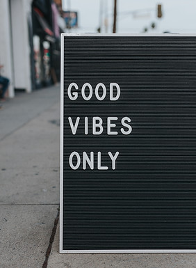 Black signboard on a pavement with white letters reading “Good Vibes Only