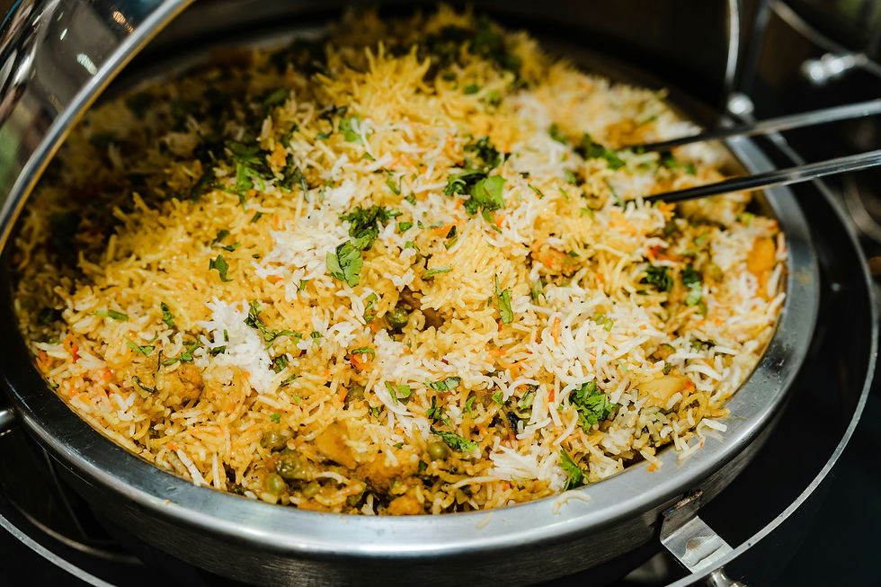 A pot of colorful biryani with vibrant yellow, white rice, and green herbs, with silver serving tongs on the side, creating a warm, appetizing scene.