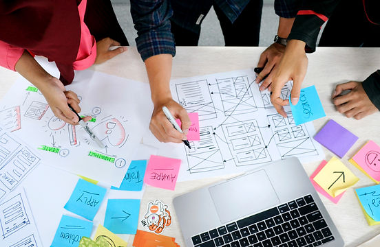 Group of business coaches standing around a table with a bunch of notes and a laptop