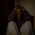 A young woman sitting on the floor with her hands holding her head looking anxious.