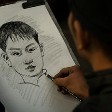 Artist sketching a detailed charcoal caricature portrait of a young man.