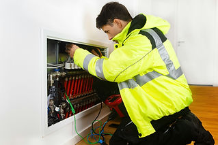 A technician inspects a complex network of pipes and cables in a utility panel