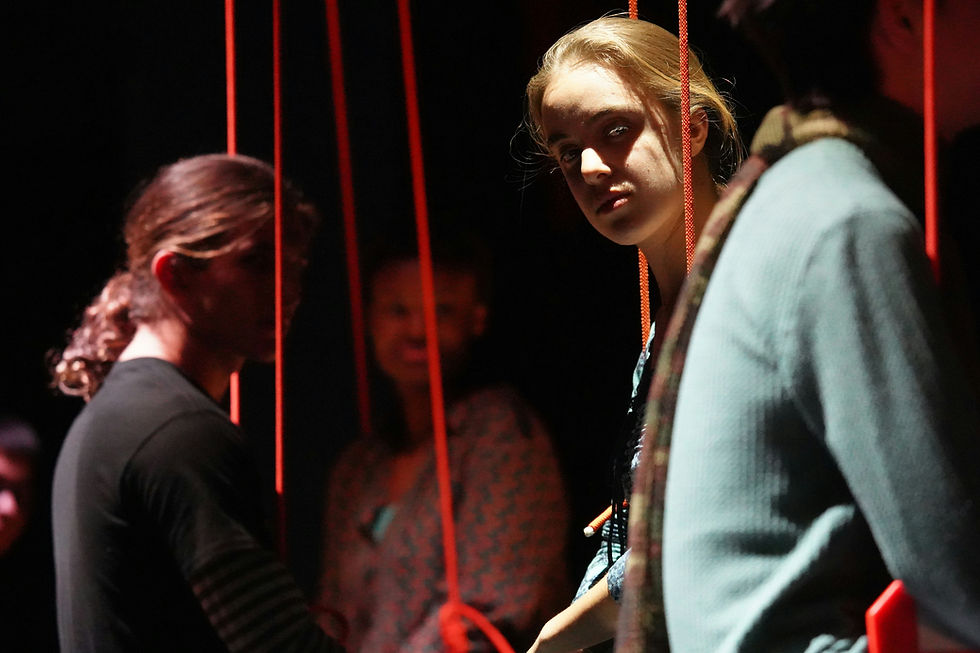 Two people framed by red cords resembling puppet strings, creating an unsettling sense of control, conformity, and performance in the workplace.