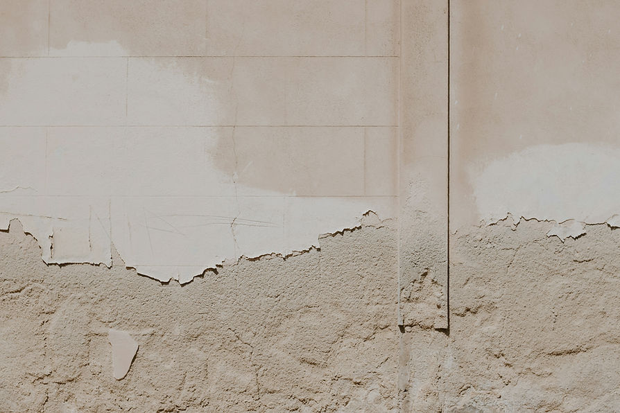 Peeling paint and crumbling plaster on a deteriorating beige wall