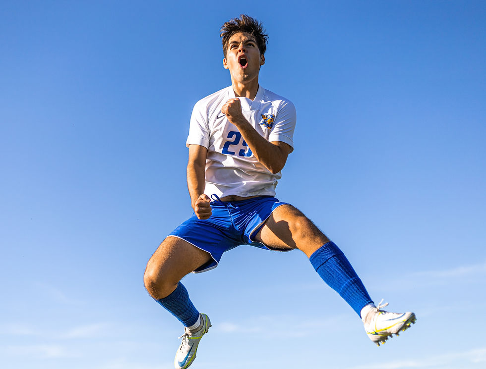 Men's footballer celebrating a goal that he's scored by jumping in the air and showing happiness