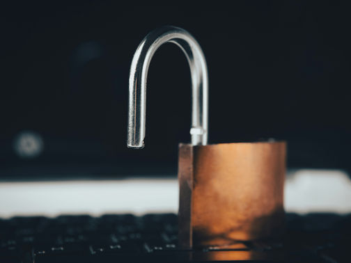 Open brass padlock resting on a laptop keyboard against a dark background, with a moody close-up look.