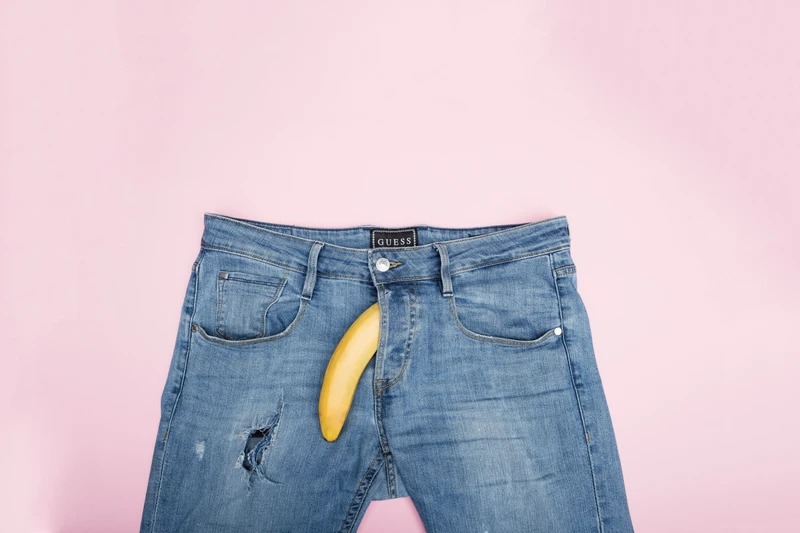 Pair of jeans on a pink background with Banana coming out of jeans fly.