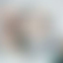 Modern lounge with grey and green chairs, a grey sofa, and black arc lamps. Glass walls and large windows create a bright, serene space.