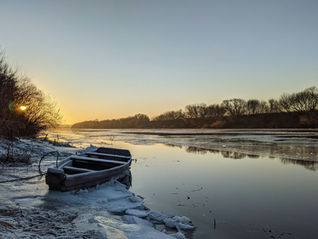A snow-covered boat resting on the edge of an icy lake.