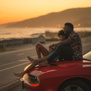 A couple sitting by the ocean, on their car