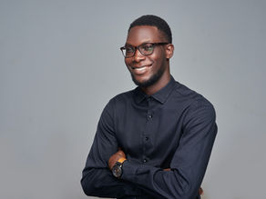 Smiling man with glasses in a dark shirt, arms crossed, posing against a plain gray studio background.